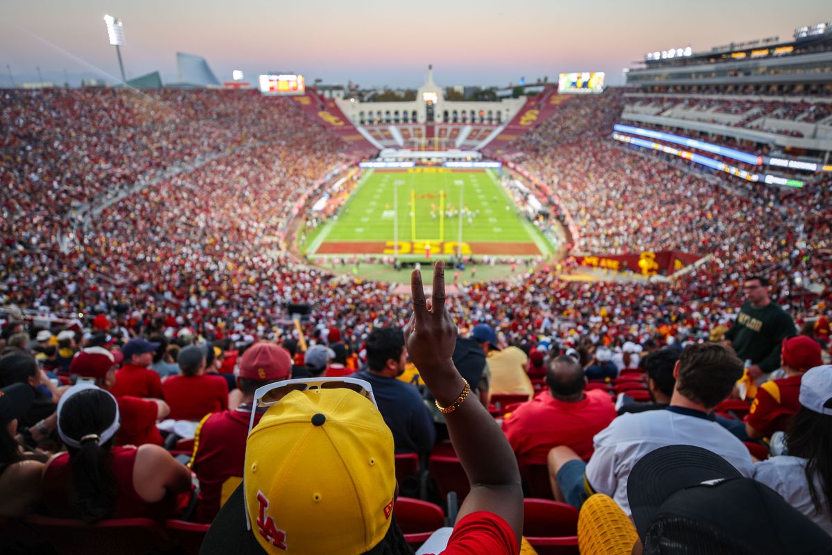 A USC fan makes the victory sign as the sun sets during a college football game against the Michigan Wolverines at the Los Angeles Coliseum on October 11, 2025 in Los Angeles, California.