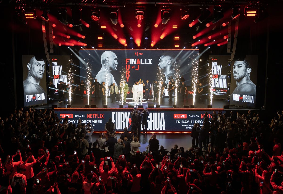 Pyrotechnics and a crowd of phone-wielding fans surround Tyson Fury and Anthony Joshua on stage at Olympia in London on Wednesday. Pyrotechnics and a crowd of phone-wielding fans surround Tyson Fury and Anthony Joshua on stage at Olympia in London on Wednesday.