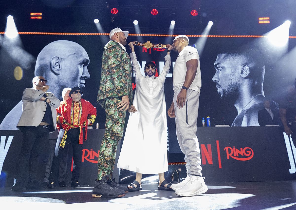 Tyson Fury and Anthony Joshua face-off as Ring Magazine owner Turki Alalshikh raises The Battle of Britain belt between them at Olympia in London on Wednesday. Tyson Fury and Anthony Joshua face-off as Ring Magazine owner Turki Alalshikh raises The Battle of Britain belt between them at Olympia in London on Wednesday.