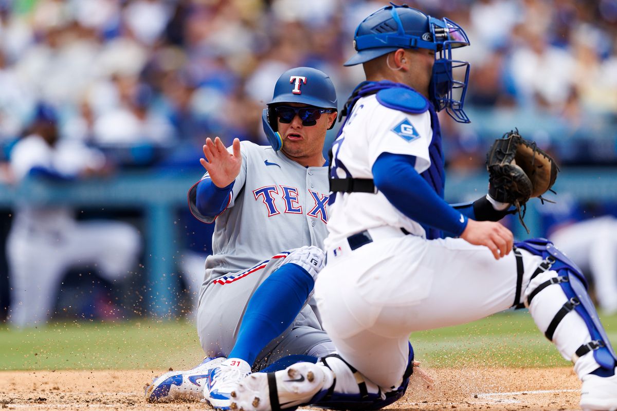 Joc Pederson #3 of the Texas Rangers slides safe into home plate against Dalton Rushing #68 of the Los Angeles Dodgers during the game at Dodger Stadium on April 12, 2026 in Los Angeles, California.