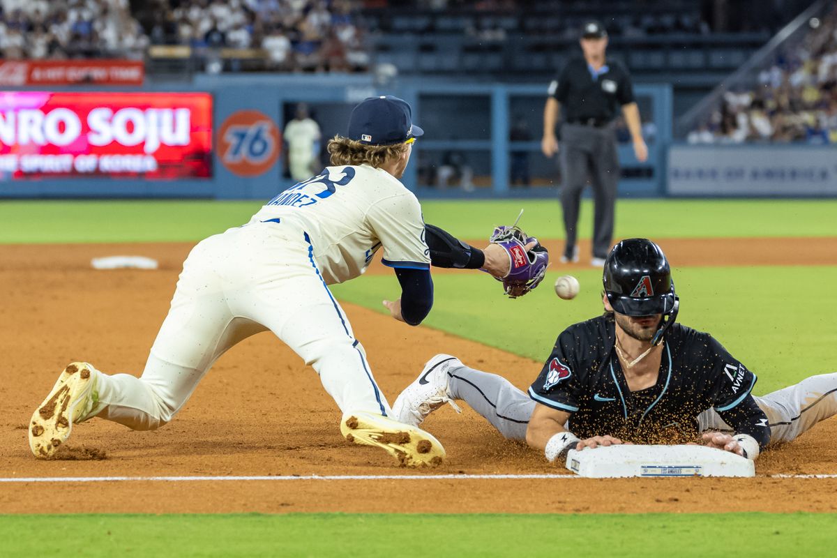 The ball sneaks past the glove of Enrique Hernández #8 of the Los Angeles Dodgers as he tries to tag Blaze Alexander #9 of the Arizona Diamondbacks during an MLB game at Dodger Stadium on August 30, 2025 in Los Angeles, California.