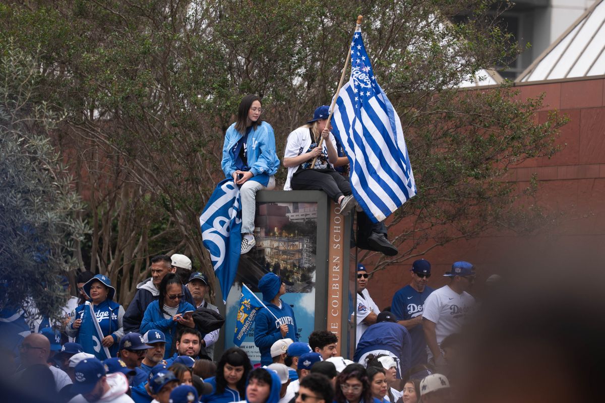 LOS ANGELES, Calif. — Nov. 3, 2025 — Dodgers fans sit atop a sign while waving team flags during the Dodgers championship parade on Monday. LOS ANGELES, Calif. — Nov. 3, 2025 — Dodgers fans sit atop a sign while waving team flags during the Dodgers championship parade on Monday.