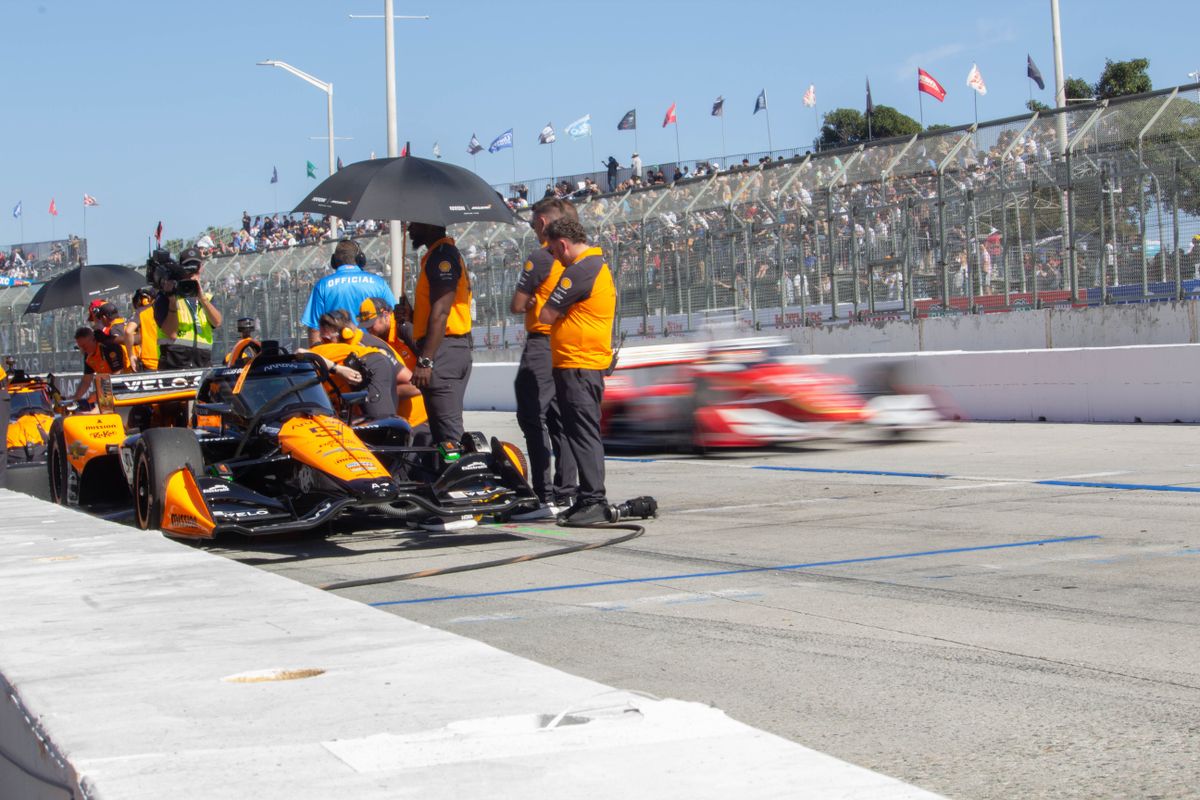 Another car races rushes past as the McLaren team tends to Pato O'Ward's car in the pit at the Friday practice sessions at the 2025 Acura Grand Prix of Long Beach. 