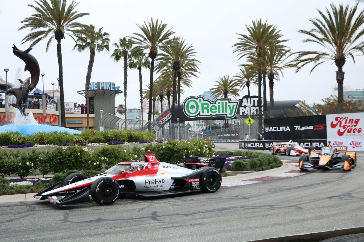 Several cars, led by Kyle Kirkwood (27), race around the Pike Outlets fountain at the 2025 Acura Grand Prix of Long Beach.