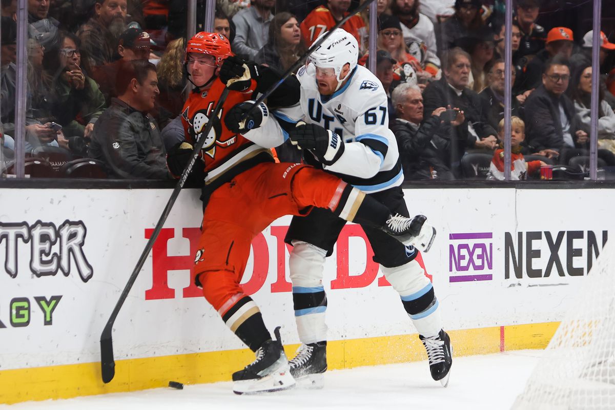 #14 D Drew Helleson of the Anaheim Ducks gets checked into the boards by #67 LW Lawson Crouse of the Utah Mammoth during an NHL game on November 17, 2025 in Anaheim, Calif.