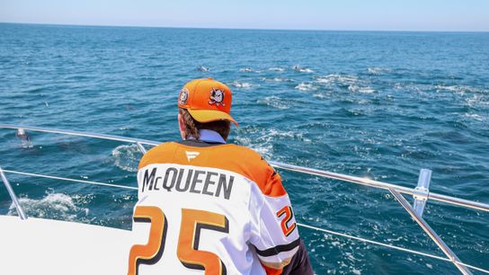 Roger McQueen taking in the sight of a group of Dolphins swimming by him and Eric Nilson on a yacht.