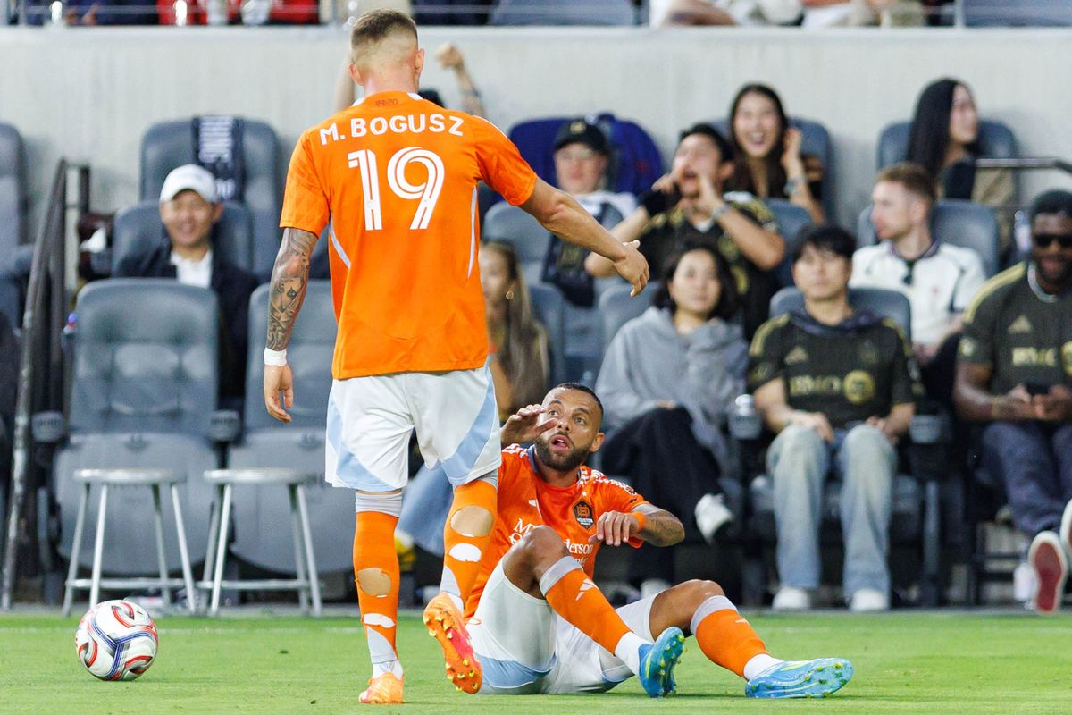 Guilherme Augusto #20 of Houston Dynamo FC gets helped up by Mateusz Bogusz #19 during an MLS match against LAFC on May 10, 2026 at BMO Stadium in Los Angeles, California.